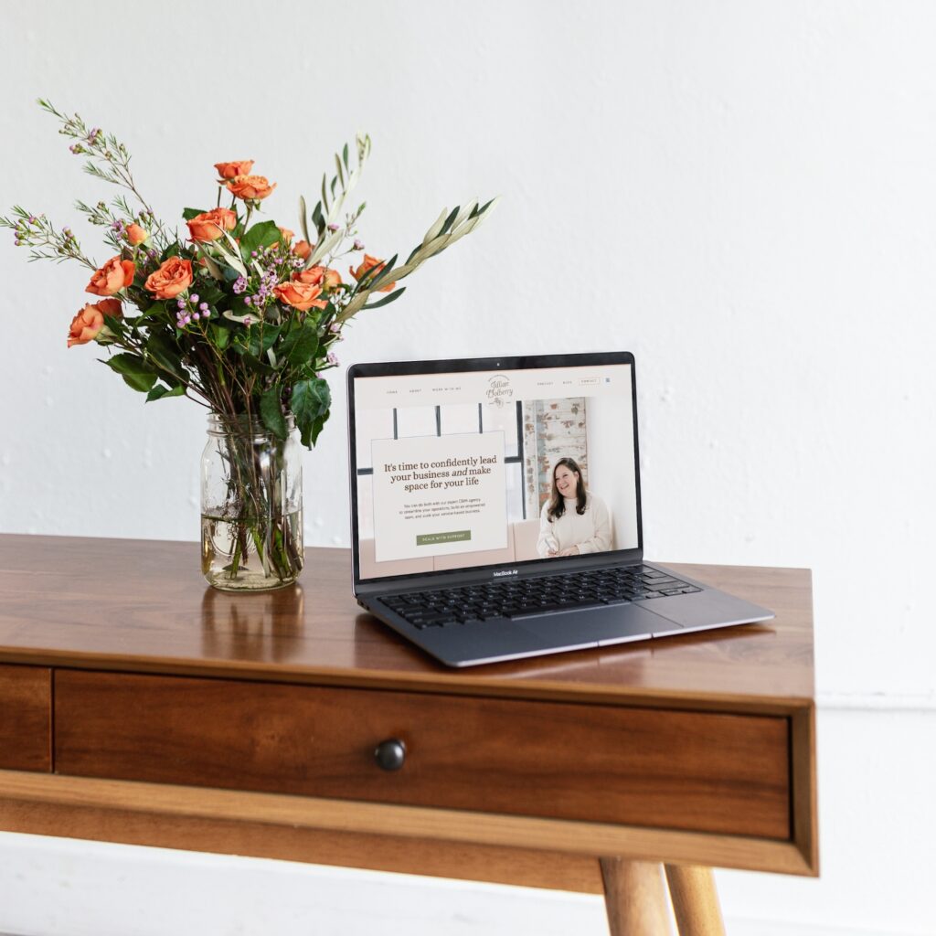 Brand design displayed on a laptop screen next to a vase of flowers on a wood table, showcasing a modern and feminine aesthetic.