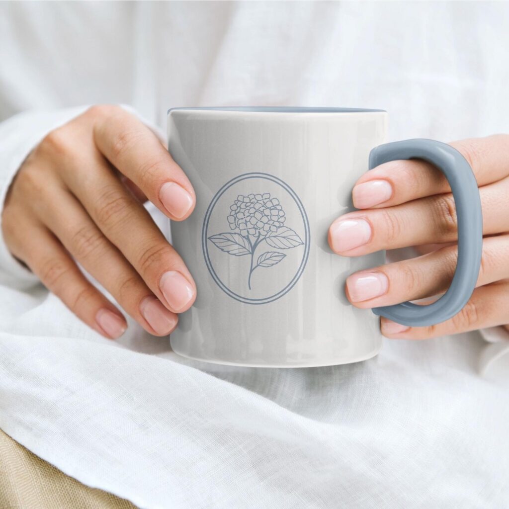 White mug featuring a floral brand icon from Jillian Dolberry’s visual identity, highlighting branded merchandise design.